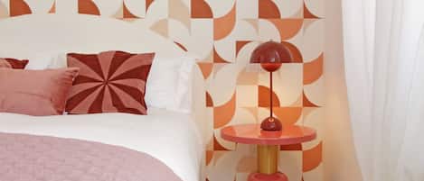 Une chambre à coucher avec un lit, des oreillers, une table ronde avec une lampe et un mur décoré de motifs.