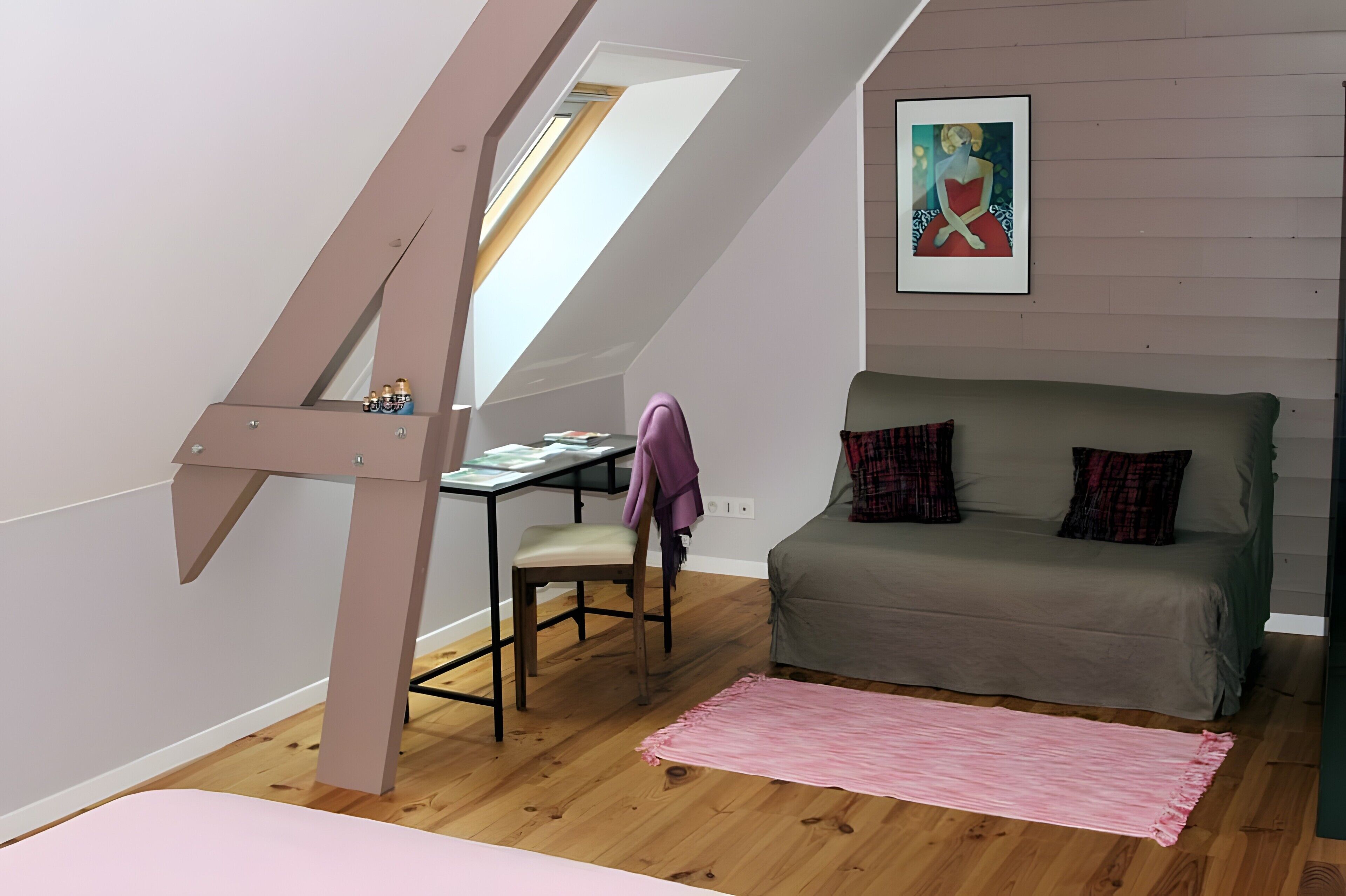 Une chambre de style « loft » avec un plafond en pente, un bureau avec une chaise, un lit avec des oreillers et un tableau accroché au mur.