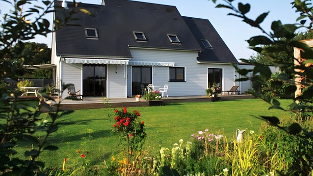A two-story house with a sloped roof, a covered porch with outdoor furniture, and a well-maintained lawn.