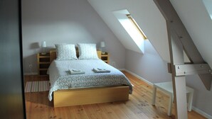 A bedroom with a sloped ceiling, a skylight, a wooden bed frame, and a bedside table with lamps.