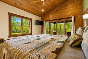 Ein Schlafzimmer mit einem großen Bett, einem Fernseher und einem Balkon mit Blick auf Bäume.