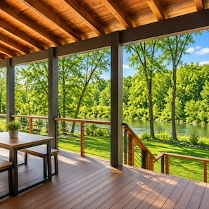 Eine Holzterrasse mit Tisch und Bänken, mit Blick auf einen See und einen Wald.