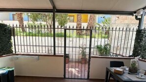 A covered patio area with a table and chairs, a view of the street outside, and a metal gate.