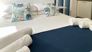 A hotel room with a striped wall, a bed with white linens, and a blue bedspread.