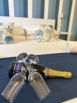 Una cama con ropa de cama a rayas y almohadas decorativas, una botella de champán y dos copas de champán sobre una superficie azul.