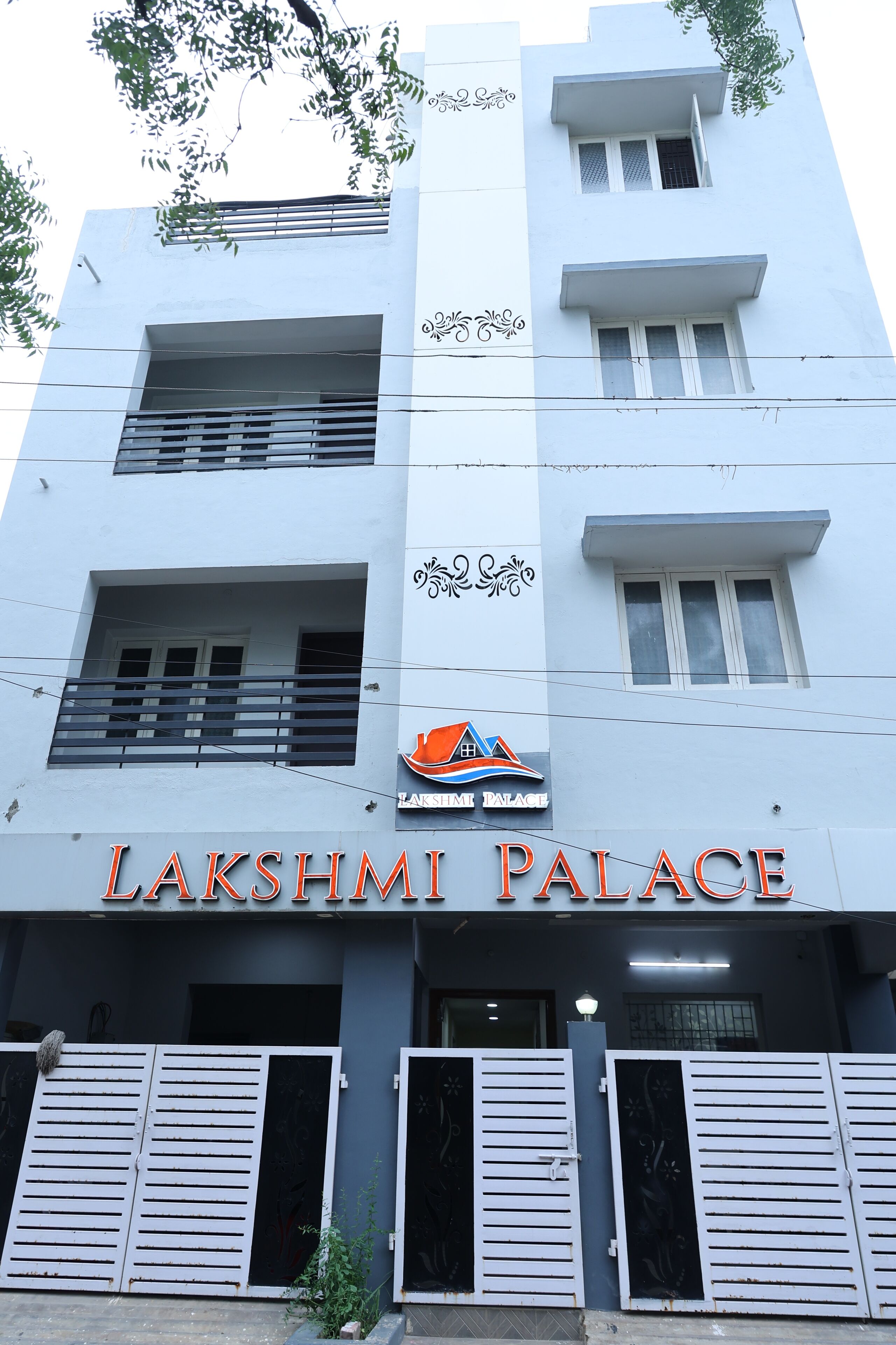 A building named Lakshmi Palace with a sign above the entrance, balconies, and a logo with a house and mountain.