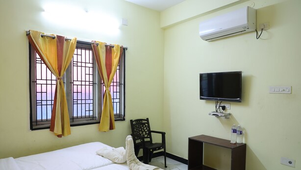 A hotel room with a bed, curtains, a chair, a TV, and a small table. - Lakshmi Palace Near MGR Bus Stand (Madurai)