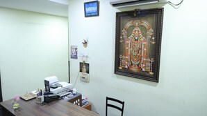 A room with a wooden desk, an air conditioner, a framed religious painting, and a small shrine. - Lakshmi Palace Near MGR Bus Stand (Madurai)