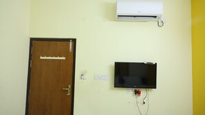 A room with a wooden door, a mounted air conditioner, and a flat-screen TV on the wall. - Lakshmi Palace Near MGR Bus Stand (Madurai)