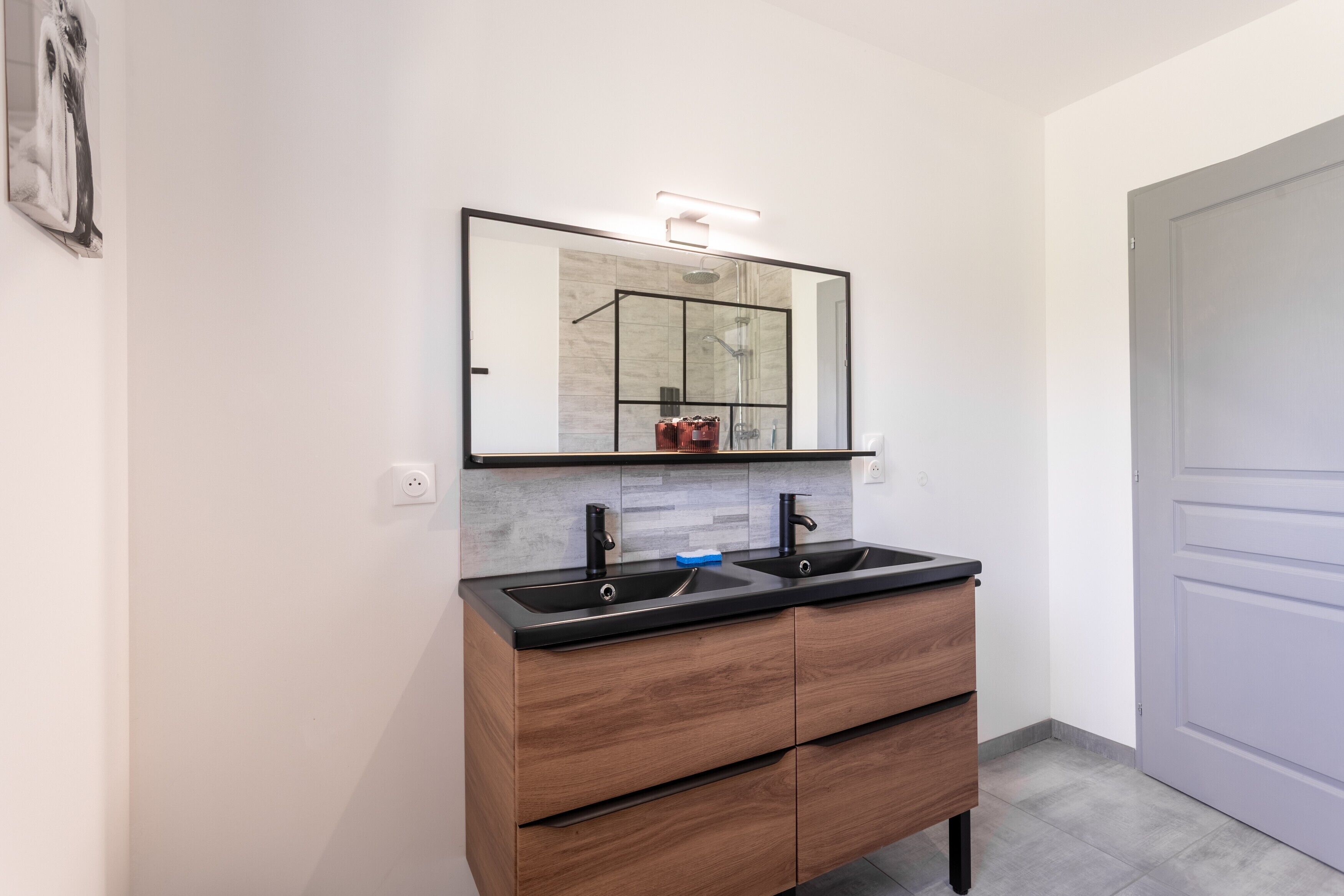 A bathroom with a double sink vanity, a mirror, and a shower area.