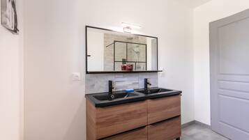 A bathroom with a double sink vanity, a mirror, and a shower area.