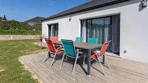 Een terras met een tafel en stoelen, een houten terras en een modern gebouw met grote ramen.