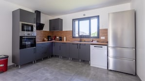 Een moderne keuken met grijze kastjes, een roestvrijstalen koelkast en een raam dat natuurlijk licht binnenlaat.