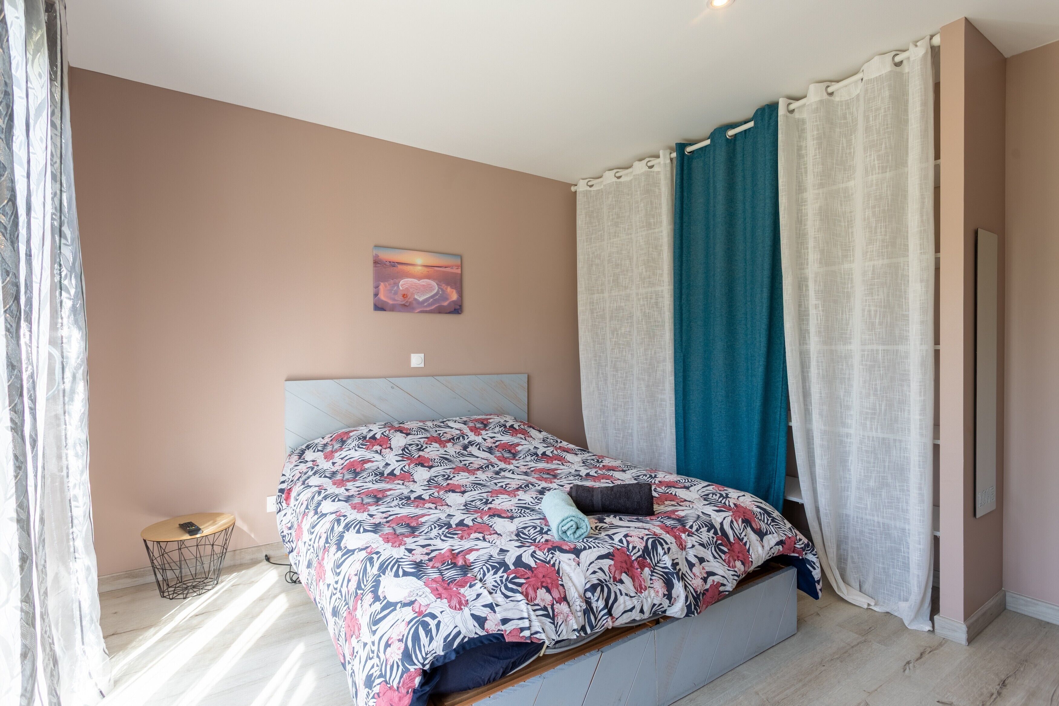 Una camera da letto con un letto, un comodino, un quadro appeso e una finestra con tende.