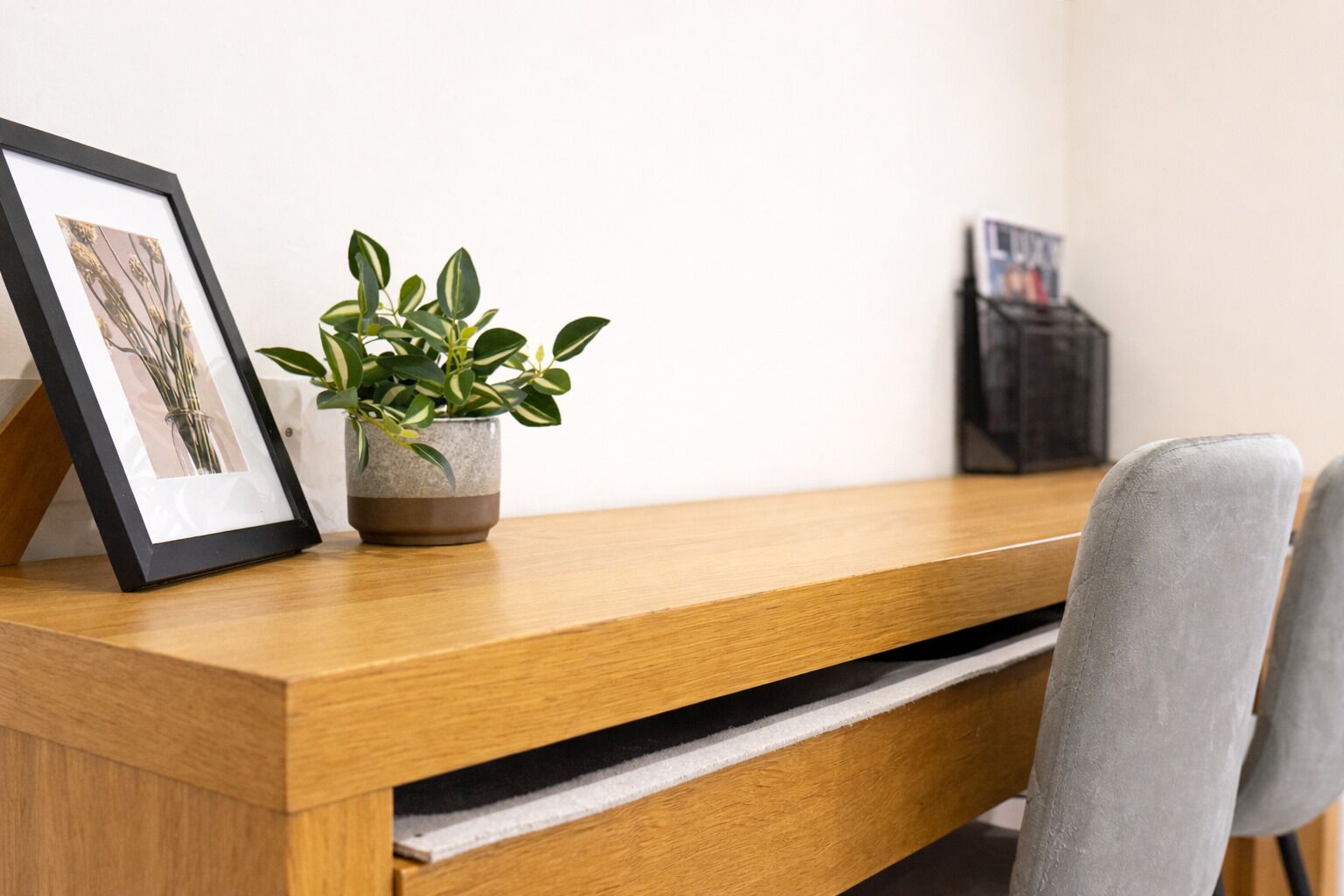 A wooden desk with a potted plant and a framed picture.