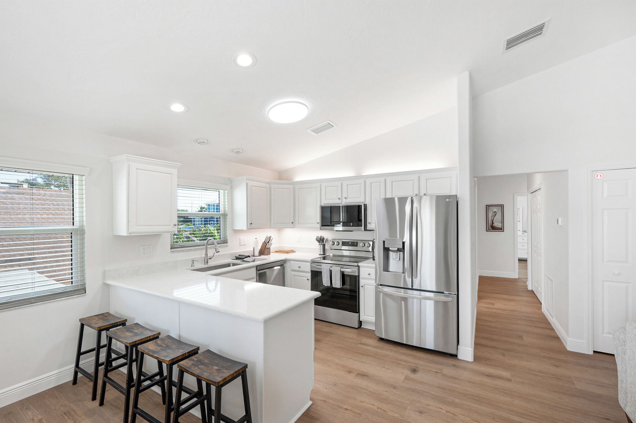 A modern kitchen with white cabinetry, stainless steel appliances, and a central island with stools.