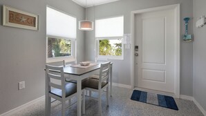 A dining area with a table and chairs, a pendant light, a door, and a window with a view of palm trees. - Cute and Cozy Island Bungalow, newly remodeled and a short walk to the beach (Holmes Beach)