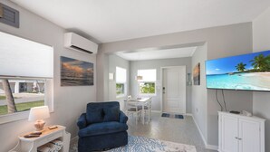 A modern living room with a blue sofa, a flat-screen TV, and a dining area with a table and chairs. - Cute and Cozy Island Bungalow, newly remodeled and a short walk to the beach (Holmes Beach)