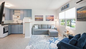 A compact living space with a kitchenette, a gray sofa, a blue couch, and artwork depicting sunsets. - Cute and Cozy Island Bungalow, newly remodeled and a short walk to the beach (Holmes Beach)