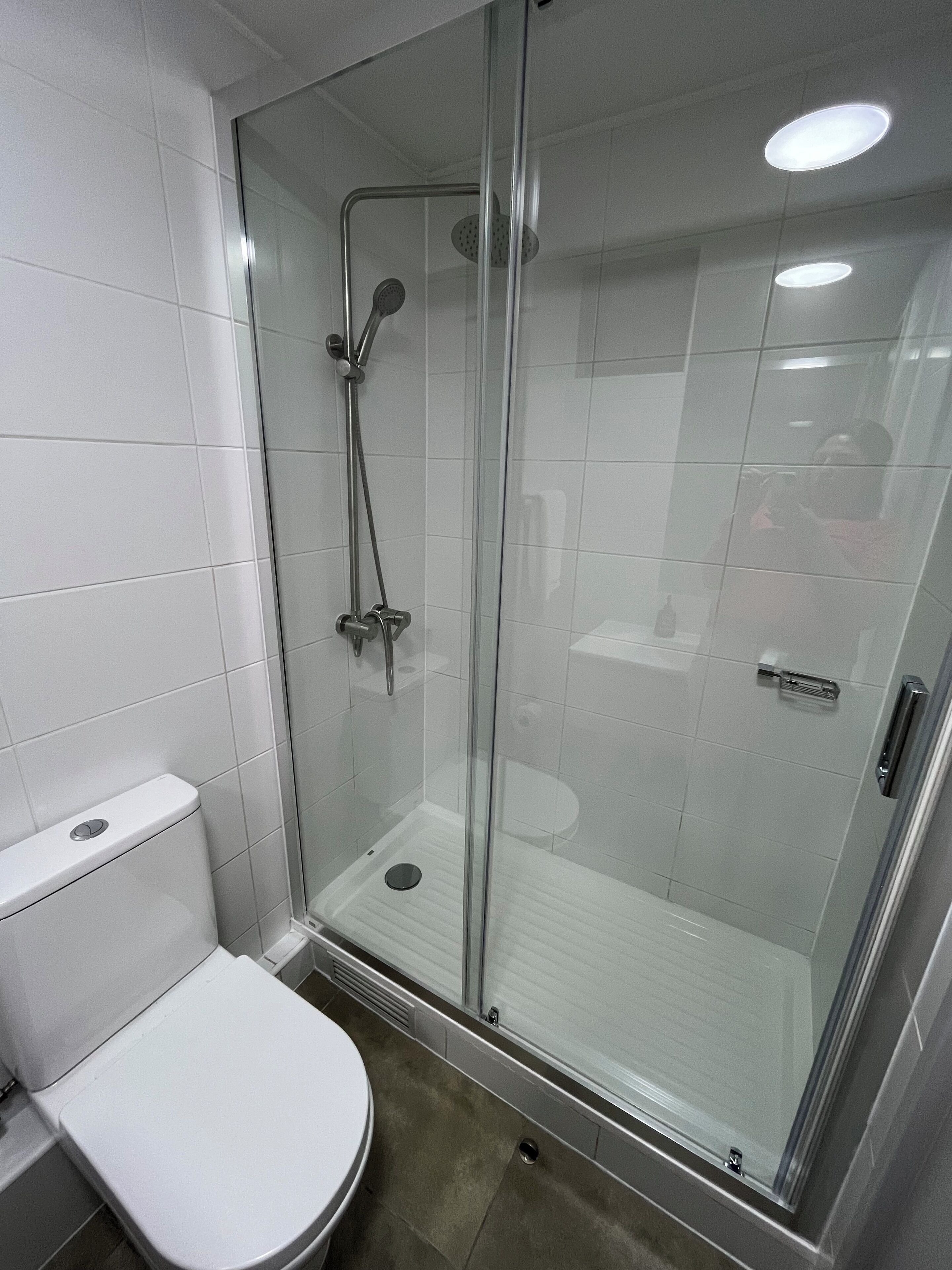Un baño moderno con ducha envuelta en vidrio, inodoro blanco y suelo de baldosas.