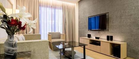 A modern living room with a glass coffee table, beige sofa, and a TV mounted on a textured wall.