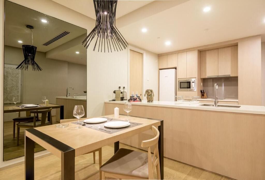 Une cuisine moderne avec des meubles en bois, un îlot central et un coin repas avec une table dressée pour deux personnes.
