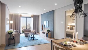 A modern hotel room with a dining area, a sofa set, a TV mounted on the wall, and a city view. - Signature Apartment at 188 Suites (Kuala Lumpur)
