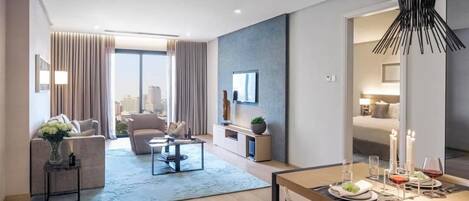 A modern hotel room with a dining area, a sofa set, a TV mounted on the wall, and a city view.