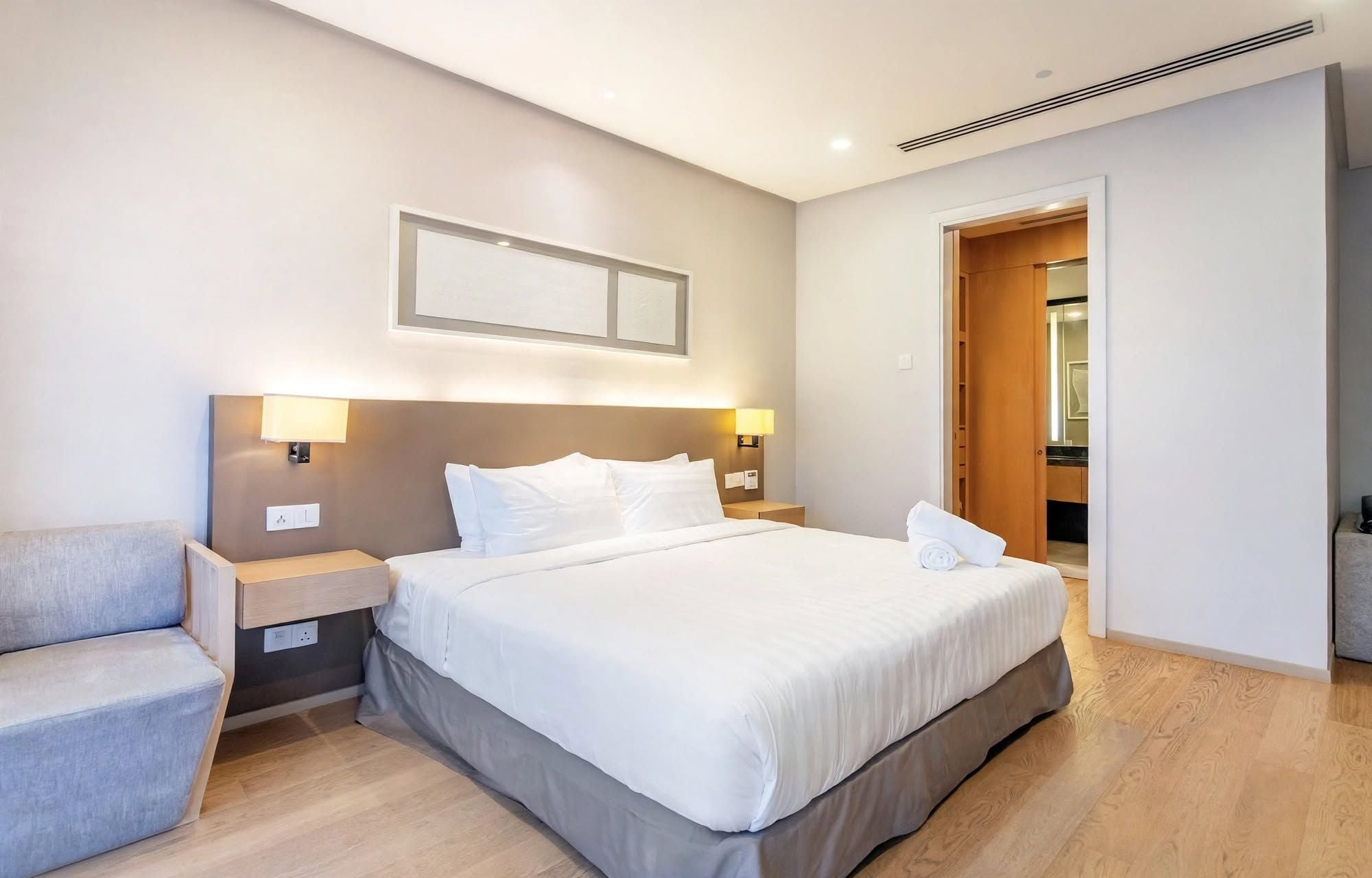 Una camera d'albergo con un letto, comodini, una sedia e una porta che conduce al bagno.