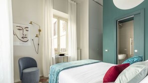 Ein Schlafzimmer mit einem Bett, einem Sessel, einem Fenster und einem durchgehenden Türspalt sichtbaren Badezimmer.