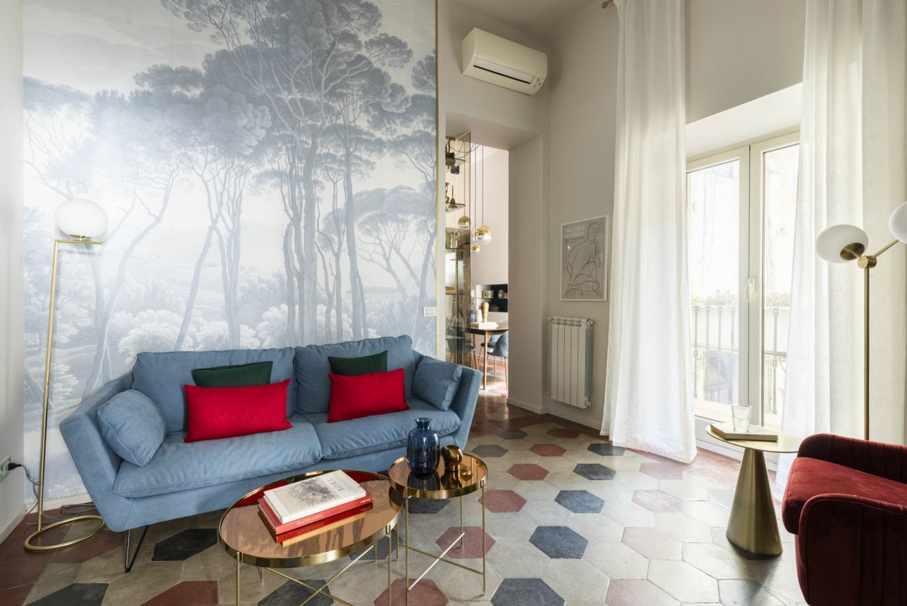 A living room with a blue sofa, red cushions, a coffee table, and a hexagonal patterned floor.