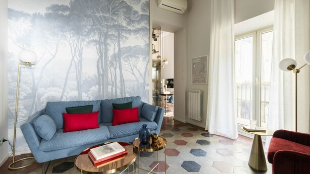 Ein Wohnzimmer mit einem blauen Sofa, roten Kissen, einem Couchtisch und einem fußbodenhohen, hexagonalen Muster.