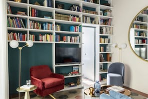 A room with a large bookshelf filled with books, a red armchair, a blue armchair, a round mirror, and a television. - Colosseo book house near Colosseo (Roma)