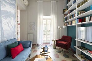 A living room with a blue sofa, a red armchair, a bookshelf, and a large window with curtains. - Colosseo book house near Colosseo (Roma)