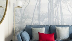 Ein Zimmer mit einem blauen Sofa, einem roten Kissen und einer Wand mit einem Baum- und Landschaftsgemälde.