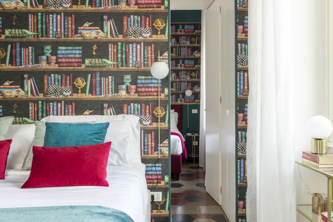 A bedroom with a large bed, multiple pillows, and a bookshelf filled with books and decorative items.