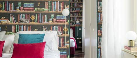 A bedroom with a large bed, multiple pillows, and a bookshelf filled with books and decorative items.