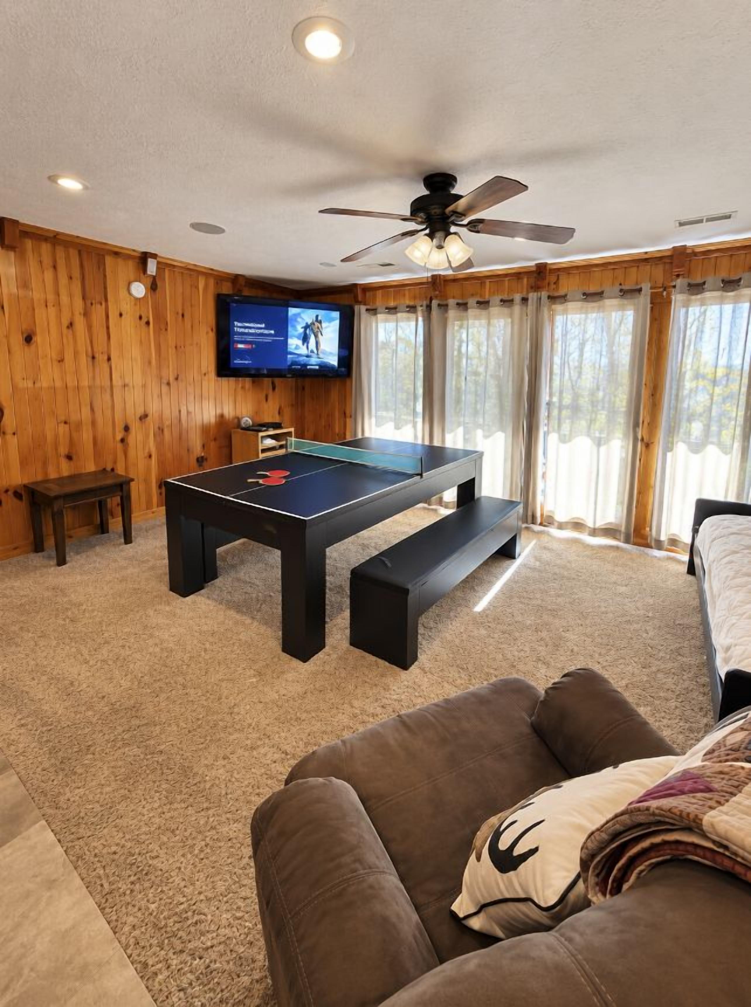 A room with a pool table, a ceiling fan, a television, and a window with curtains.