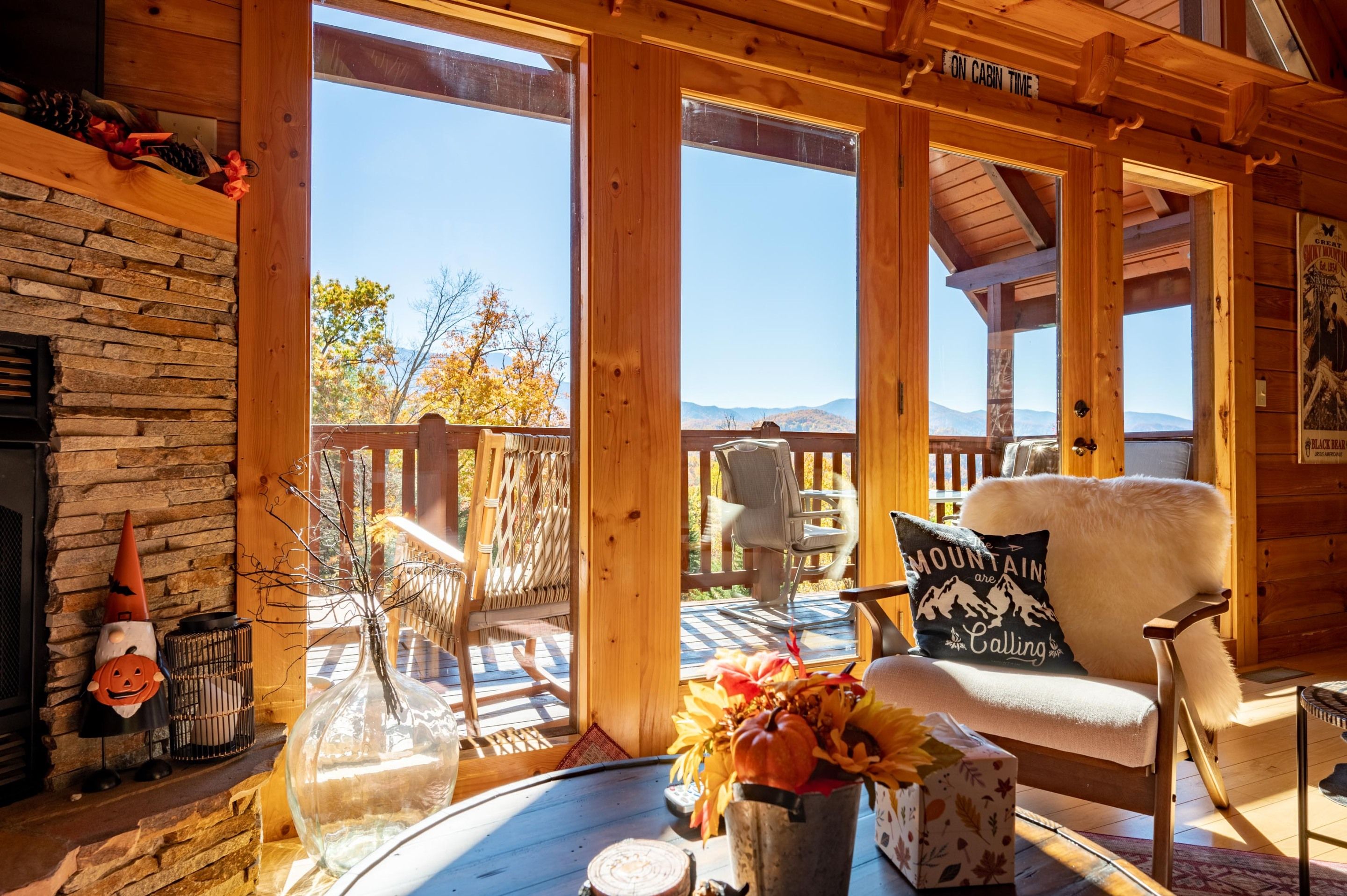 Interior acogedor de una cabaña con chimenea de piedra, terraza de madera y vista a las montañas.
