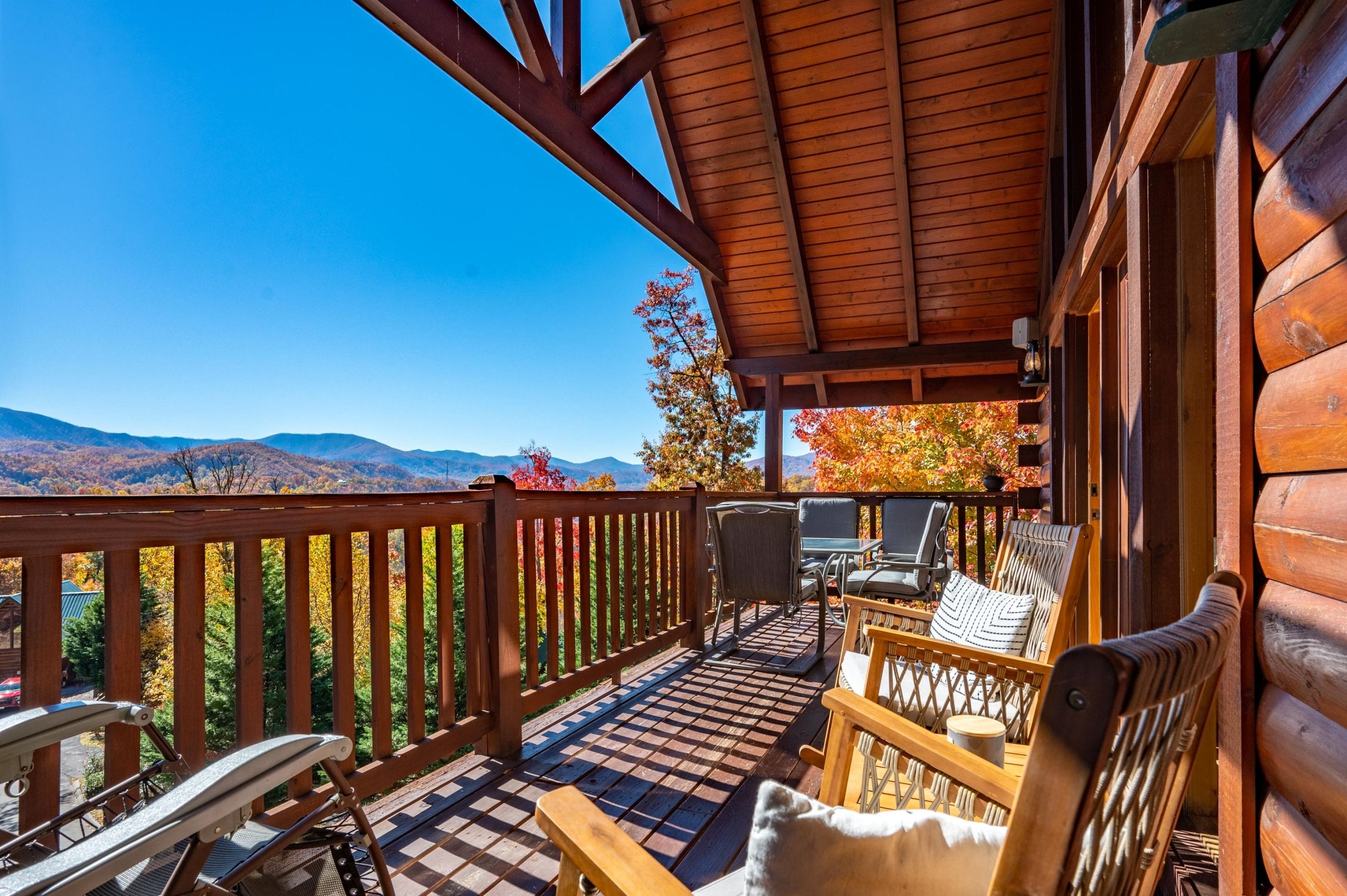 A wooden deck with outdoor furniture, a view of mountains, and a clear sky.