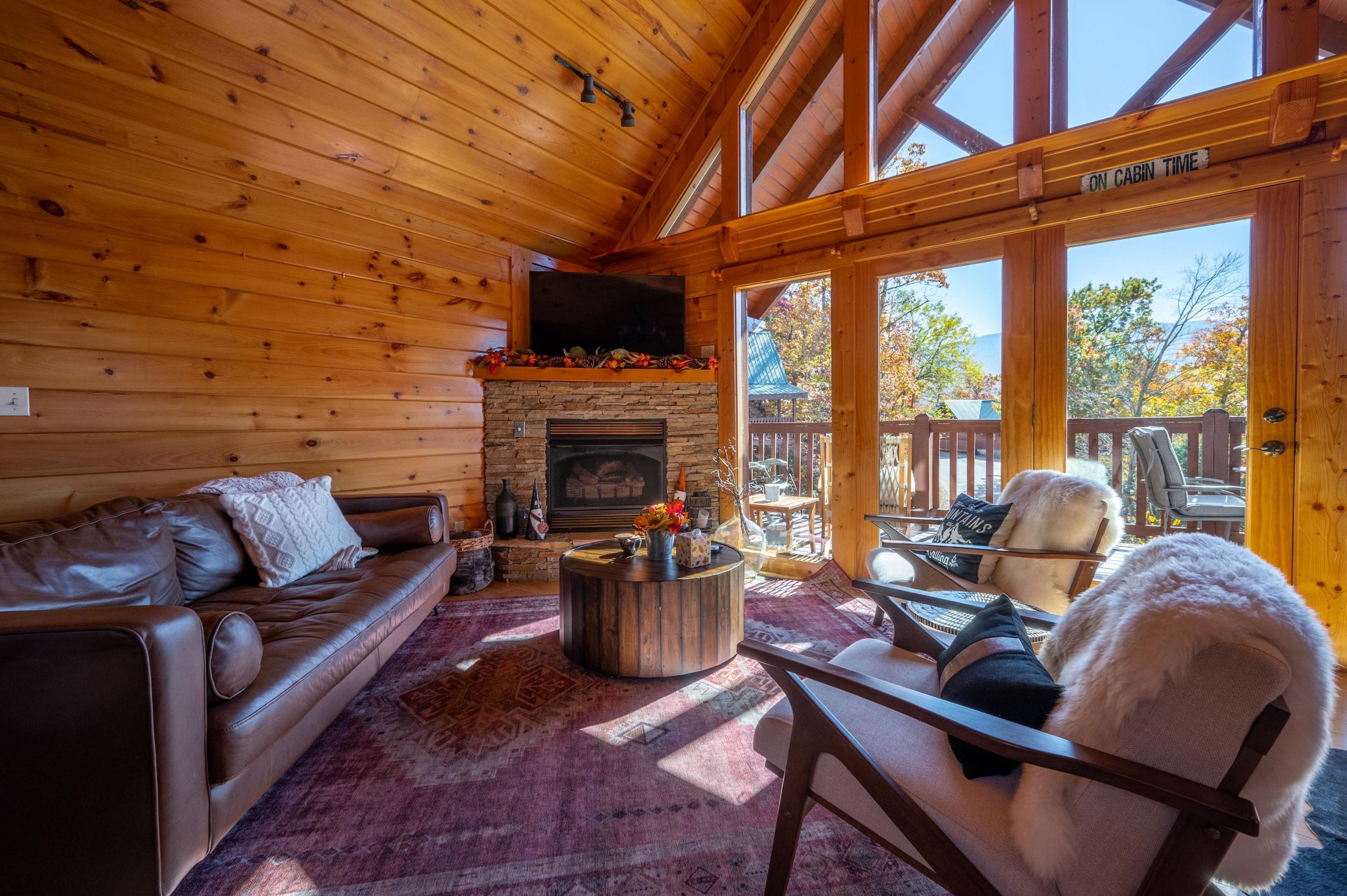 A wooden cabin interior with a fireplace, leather sofa, and a view of the outdoors.