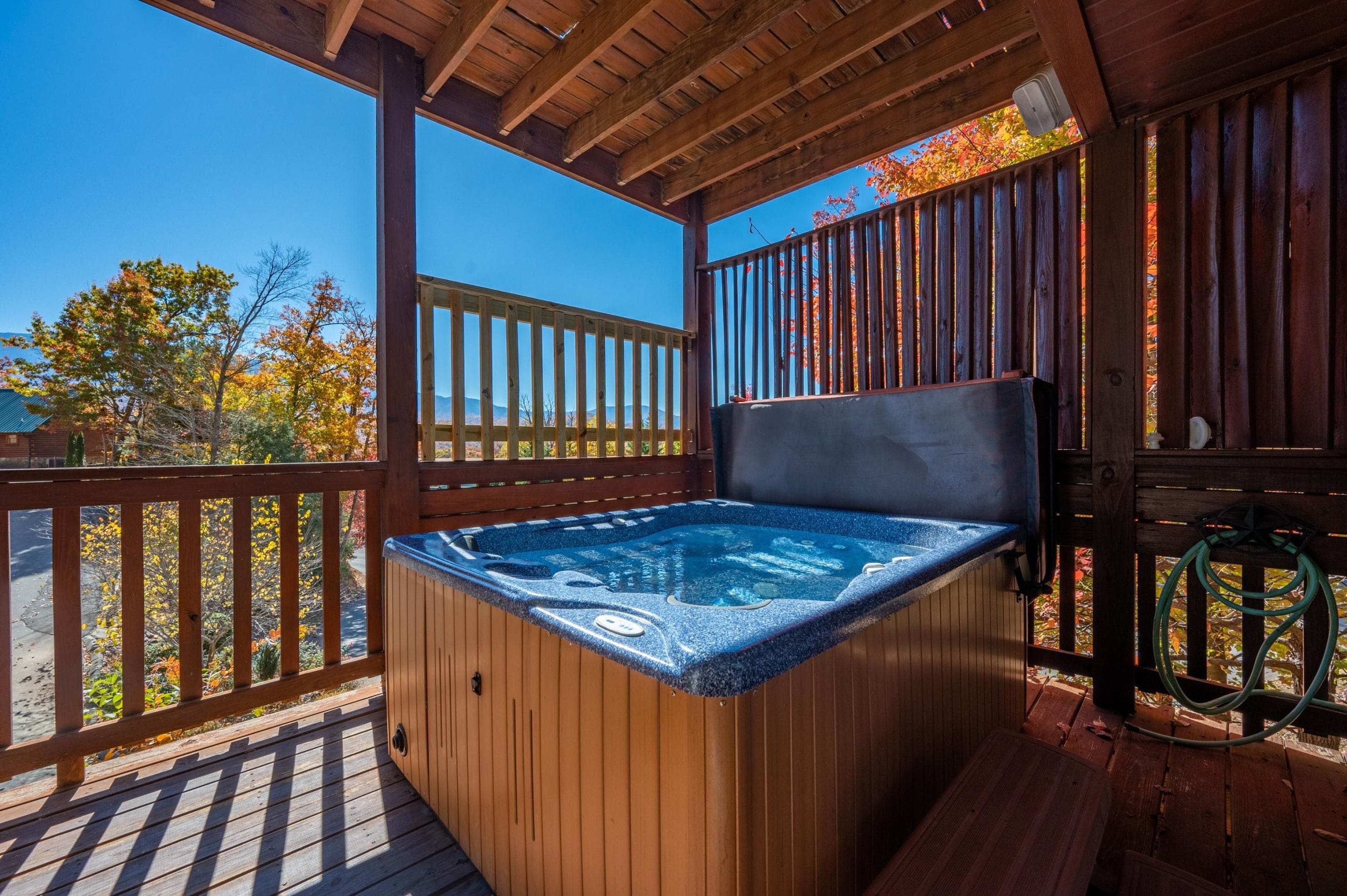 A wooden deck with a hot tub, wooden railings, and a clear view of autumn trees.