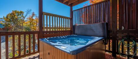 A wooden deck with a hot tub, wooden railings, and a clear view of autumn trees.