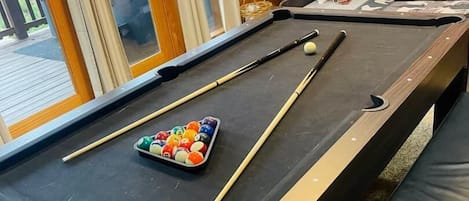A pool table with balls and cues, a bench, and a bunk bed in a room with wooden walls and a glass door.