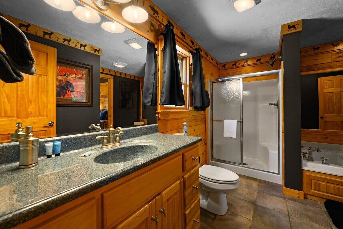 A bathroom with a granite countertop, wooden cabinets, a toilet, and a glass-enclosed shower.