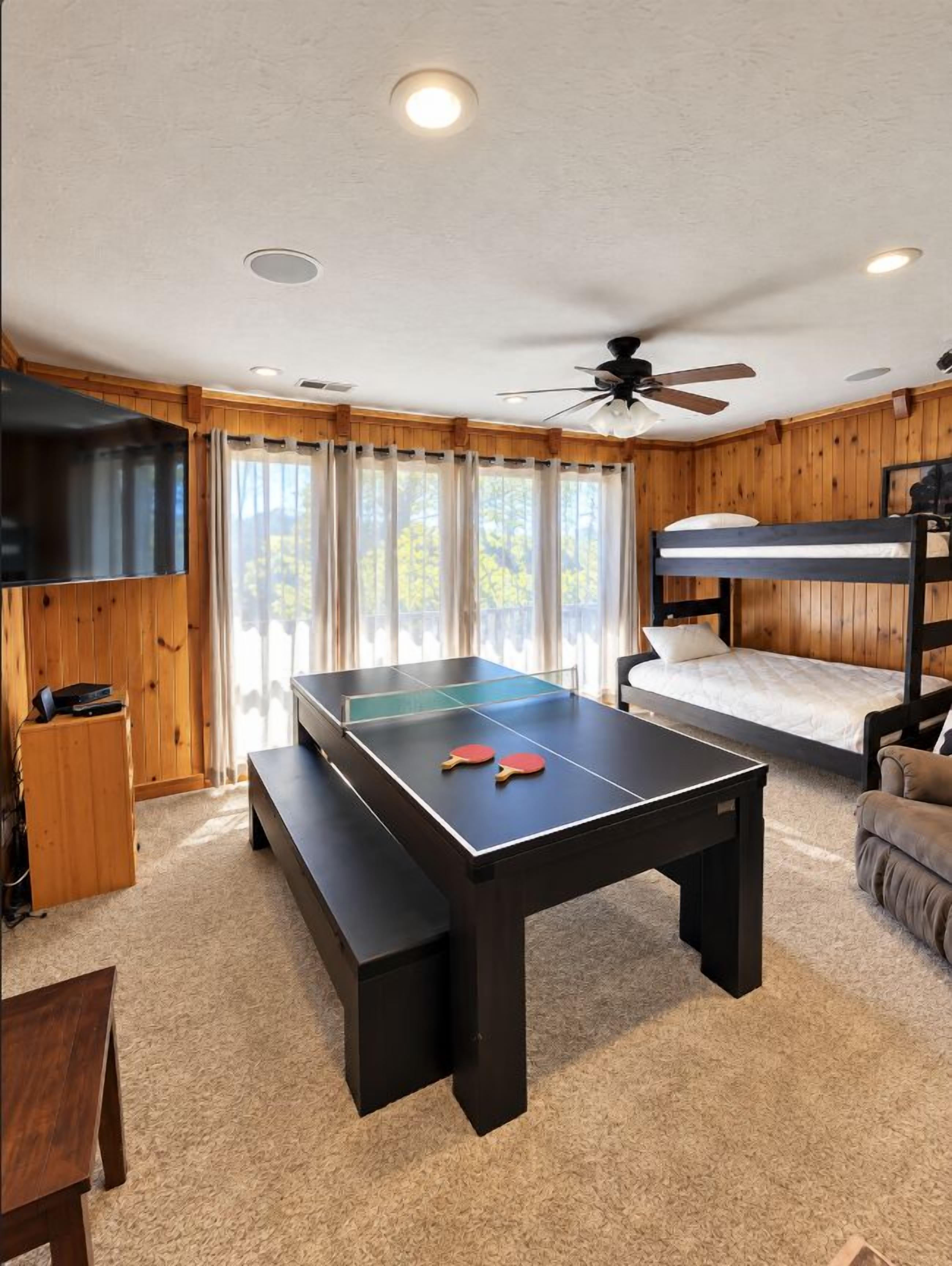 Una habitación con mesa de ping pong, ventilador de techo, cama litera y televisor.