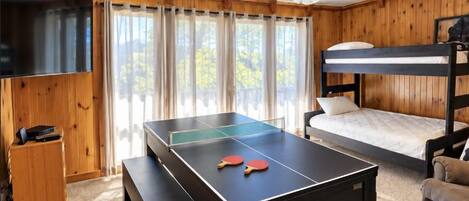 Una habitación con mesa de ping pong, ventilador de techo, cama litera y televisor.