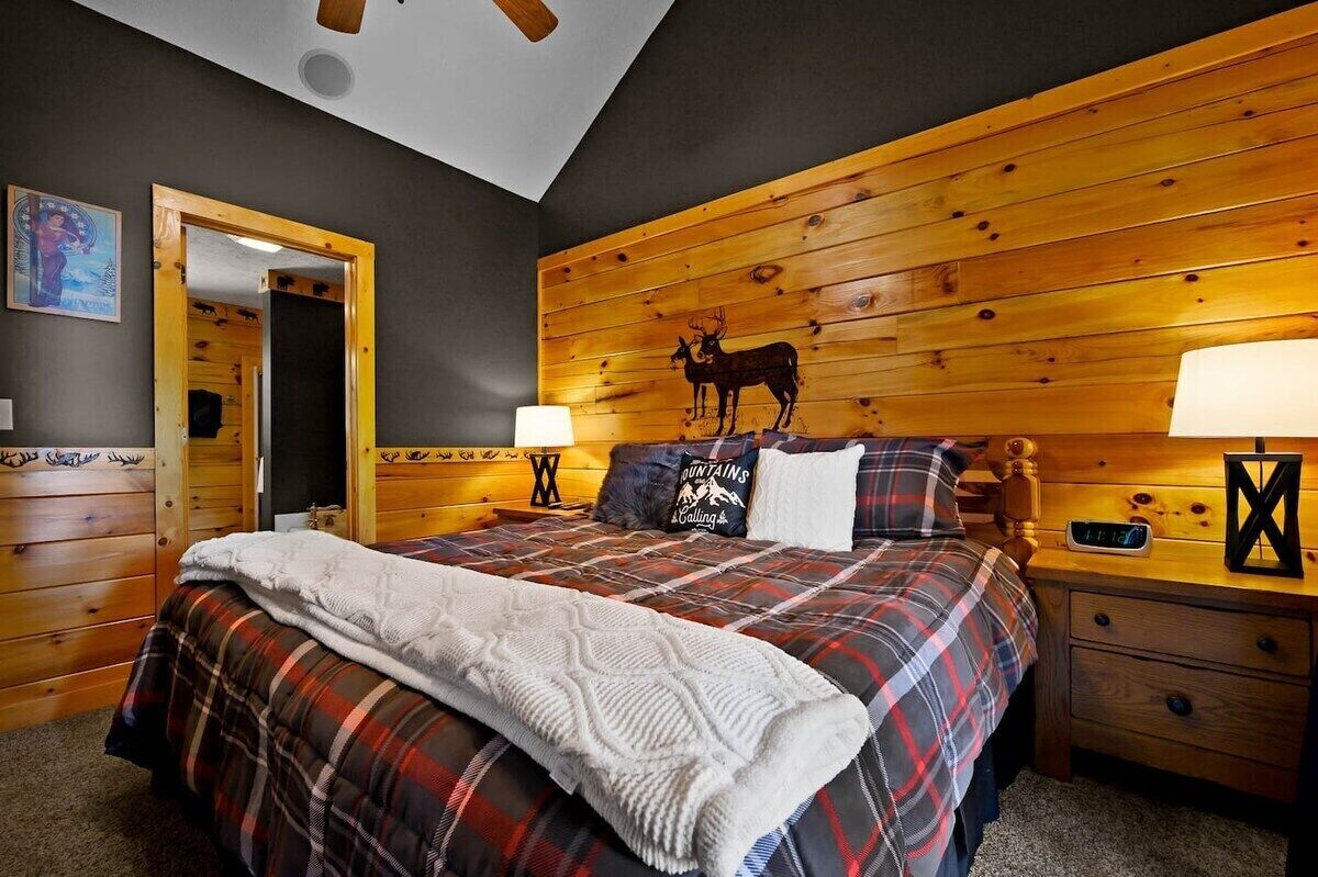 A cozy bedroom with a wooden headboard, a bed with plaid bedding, two bedside lamps, and a nightstand with a clock.