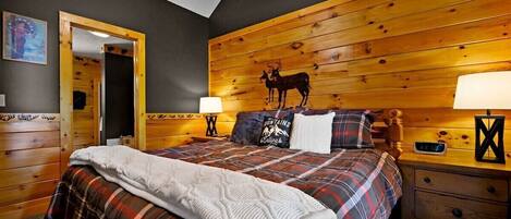 A cozy bedroom with a wooden headboard, a bed with plaid bedding, two bedside lamps, and a nightstand with a clock.