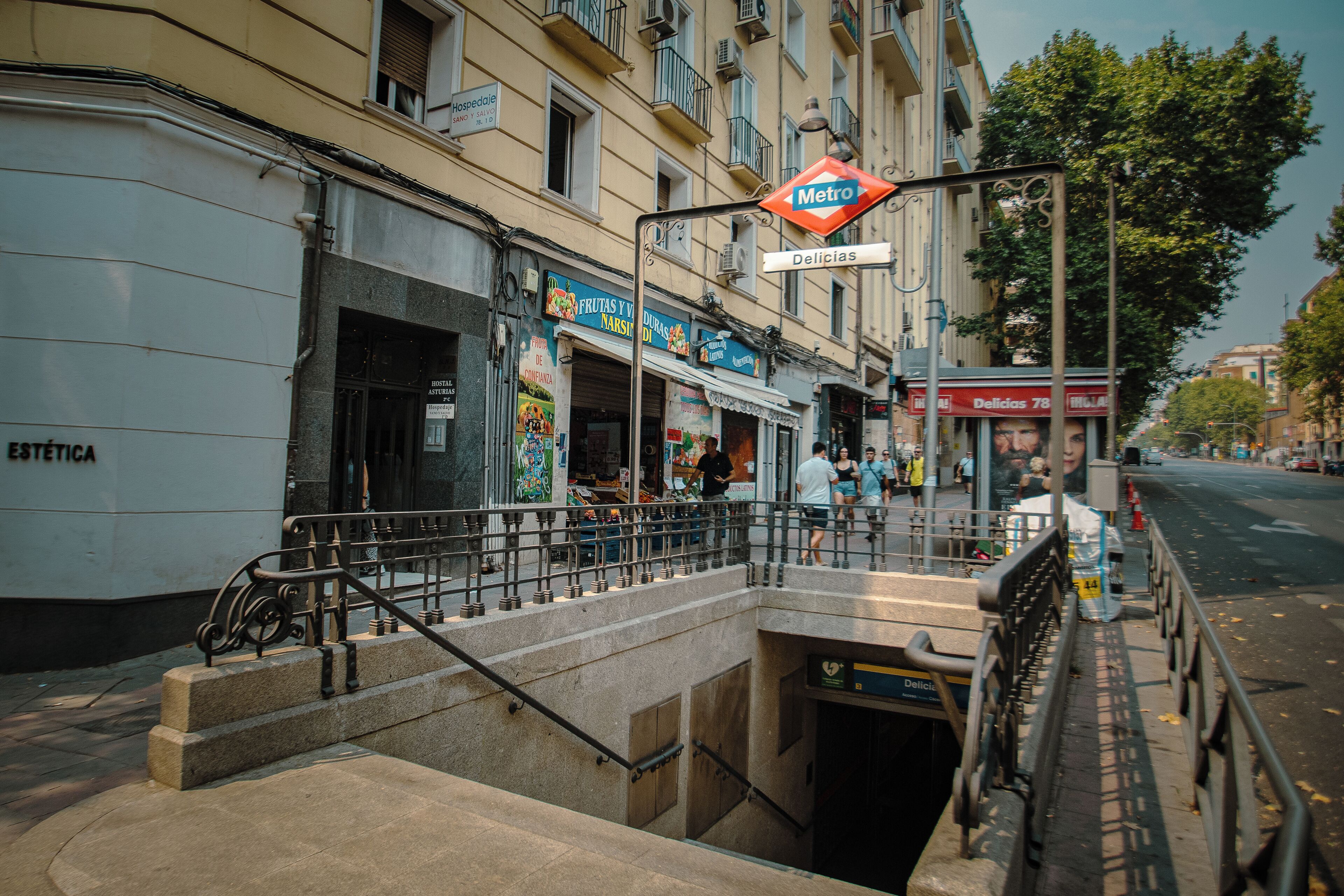 Eine Metrostation mit einer Treppe zu einem Bahnsteig, umgeben von Geschäften und Gebäuden.